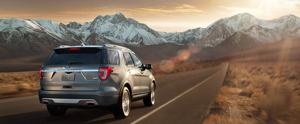 SUV driving on mountain road at sunset, showcasing a scenic snowy mountain backdrop.