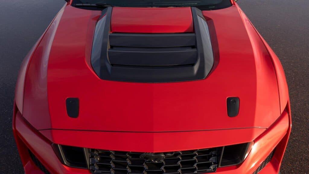 Red car hood with prominent air vents and sleek detailing on a smooth surface.