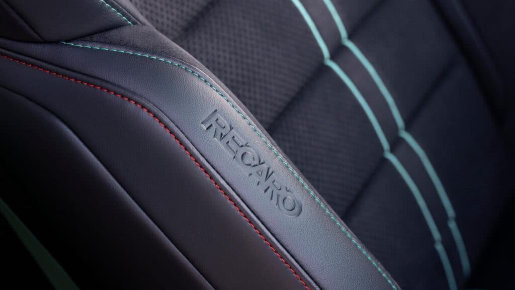 Close-up of Recaro car seat with detailed red and teal stitching on black leather.