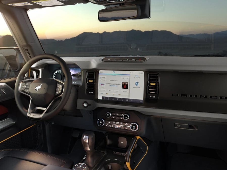 Modern SUV interior with steering wheel, touchscreen display, and dashboard controls at sunset.