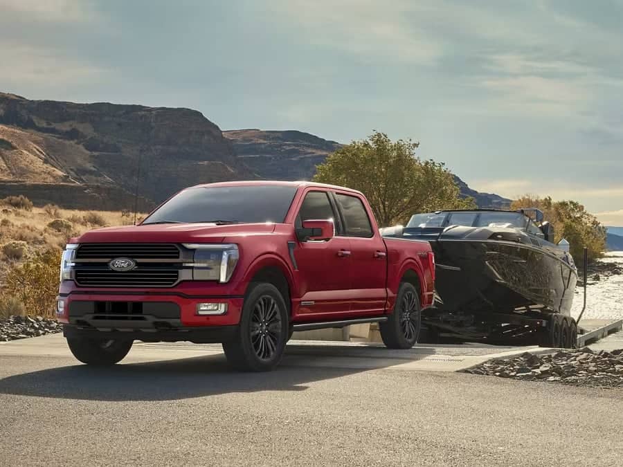 Red Ford truck towing a boat at a scenic lakeside location with mountains in the background.