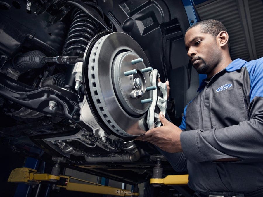 Mechanic inspecting a car brake disc and caliper in a garage setting.
