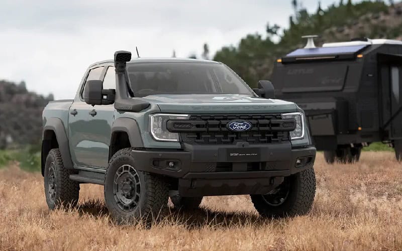 Ford pickup truck parked on grassy terrain with a trailer in the background, under a cloudy sky.