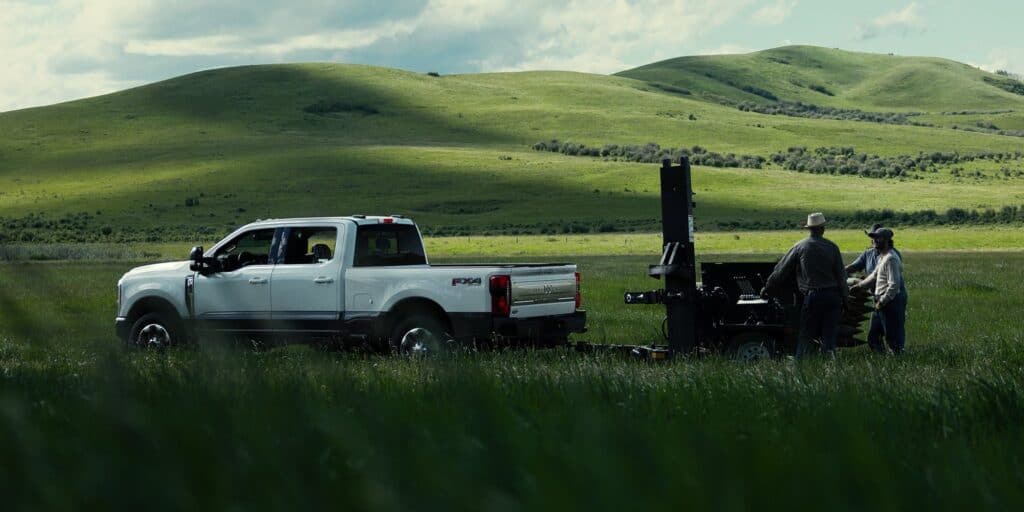2027 Ford F-250 side view of white pickup towing equipment across green grassy field