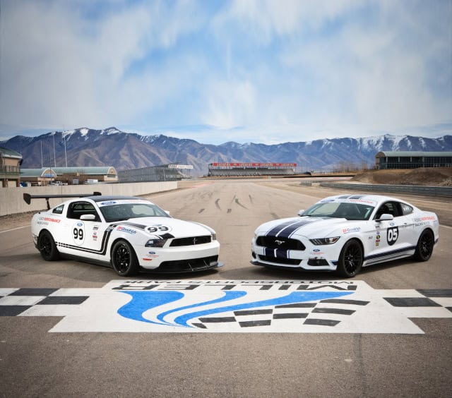 Two Ford Mustang race cars, numbers 99 and 05, on a track with mountain backdrop.